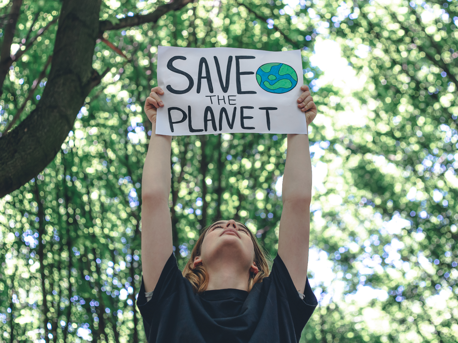 Junger Mensch hält im Wald ein Schild in die Luft, mit der Aufschrift: Save the Planet